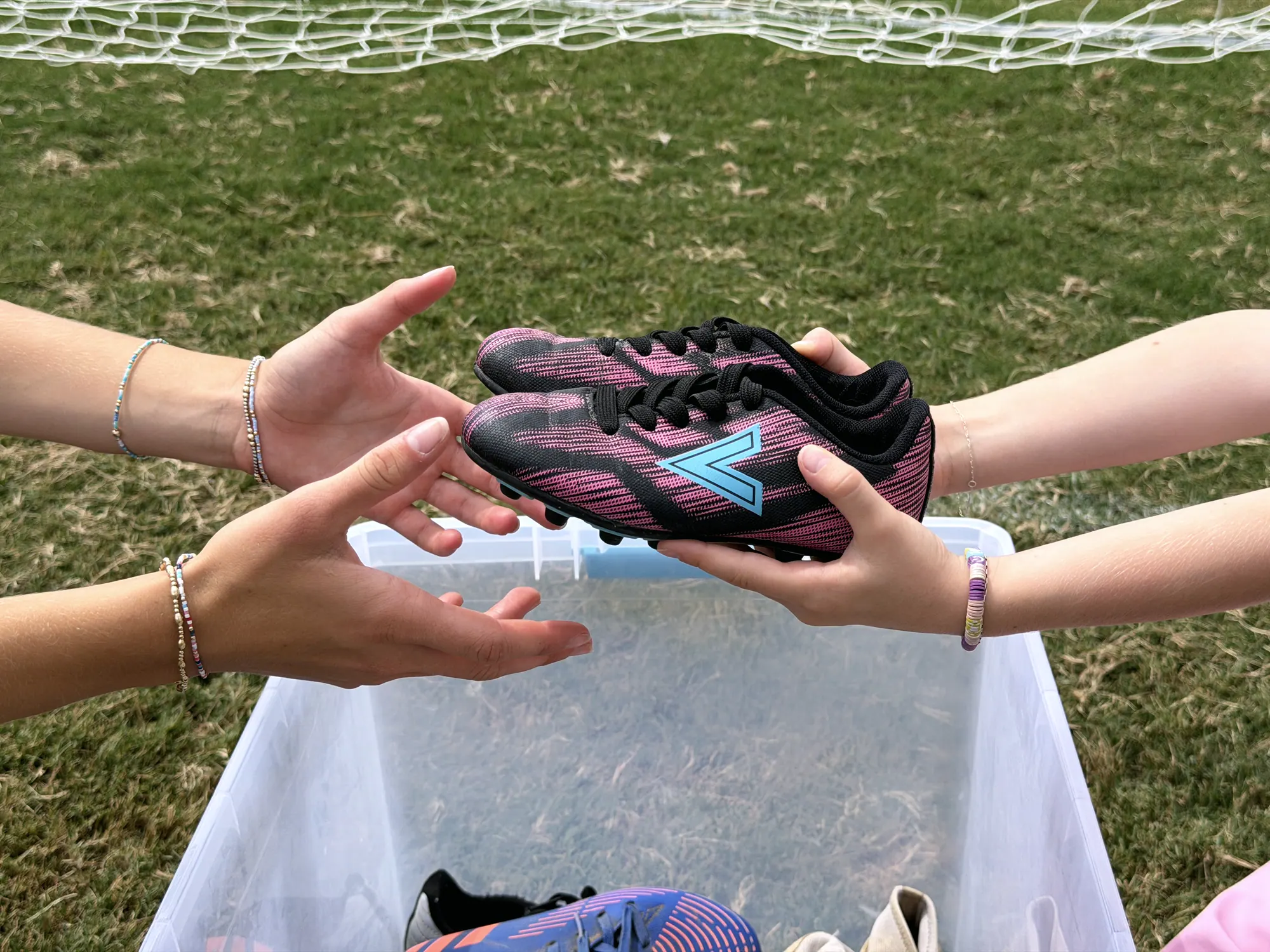 A worn cleat passing from one pair of hands to another over an open donation bin